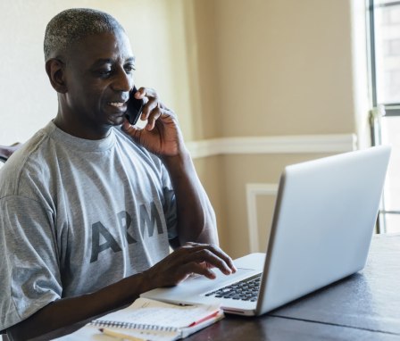 Person in Army shirt talking on the phone and looking at a laptop