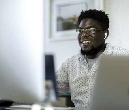 Man smiling at computer monitor and laptop