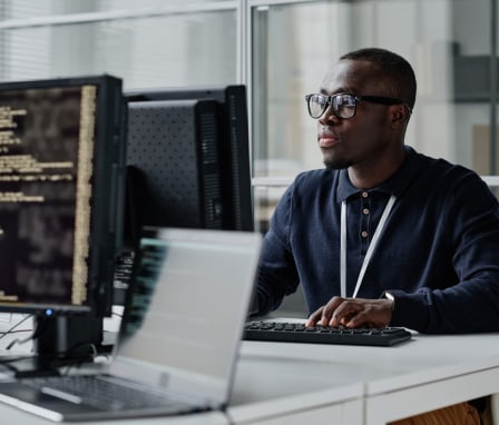 African American young developer in eyeglasses concentrating on his online work on computer sitting at workplace