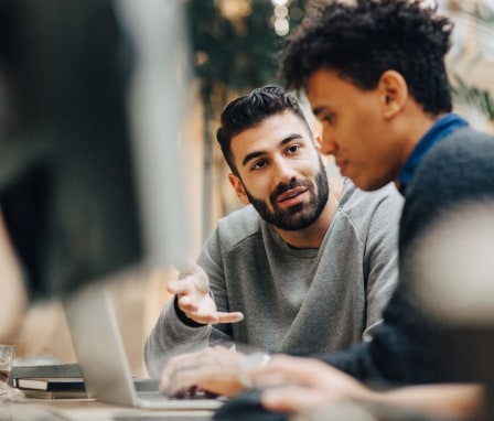 Two men talking while working on computers